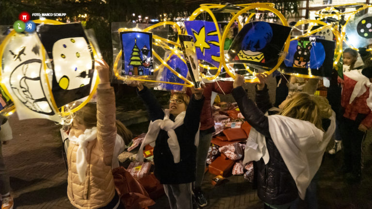 Cadeaus en lichtobjecten neergelegd onder feestelijk ontstoken kaaskerstboom