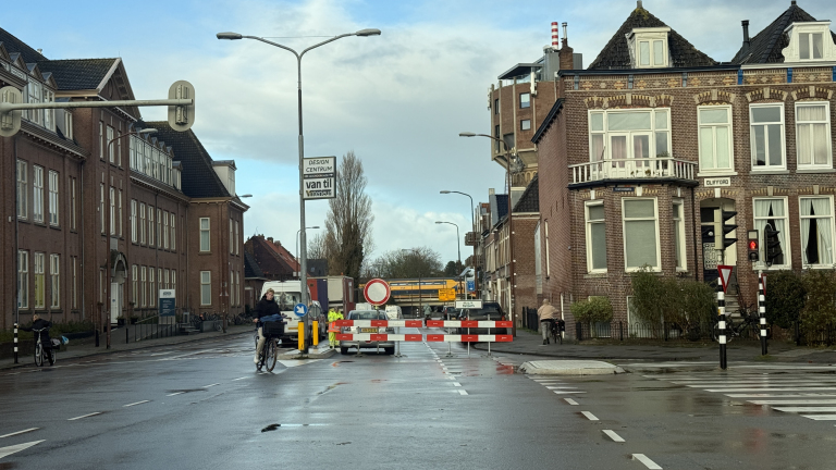 Straat met wegafsluiting, auto's, fietsers en historische gebouwen aan beide zijden.