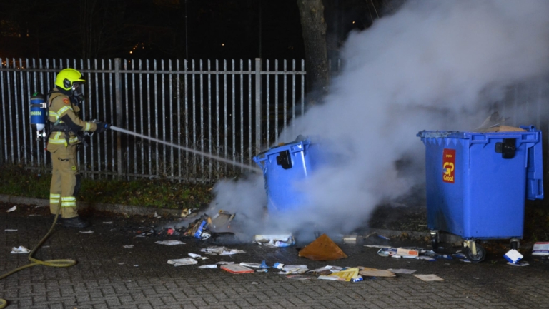 Brandweerman dooft brand in afvalcontainer met rookontwikkeling.