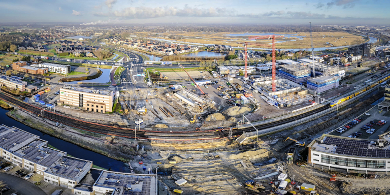 Luchtfoto van een bouwplaats in een stedelijke omgeving met wegen, treinrails en huizen.