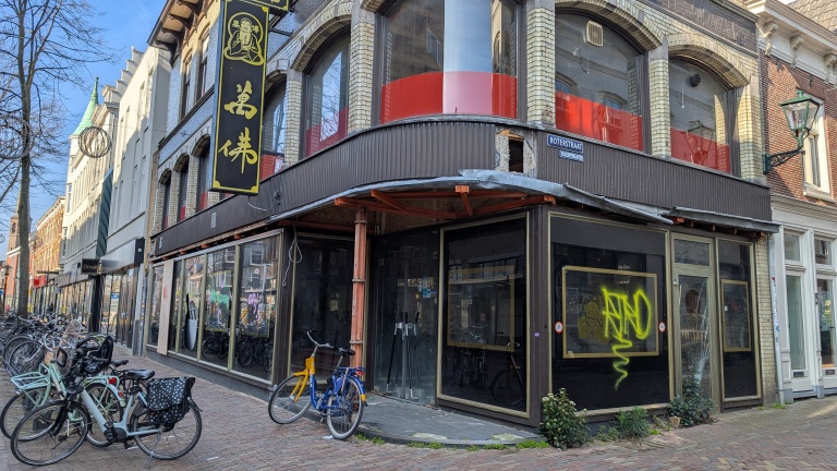 Buitenaanzicht van een Chinees restaurant aan de Boterstraat met gele graffiti op het raam en fietsen langs de straat.