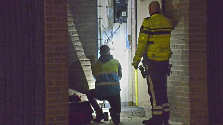 Een politieagent en een persoon in een veiligheidshesje inspecteren een elektriciteitskast in een donkere gang.