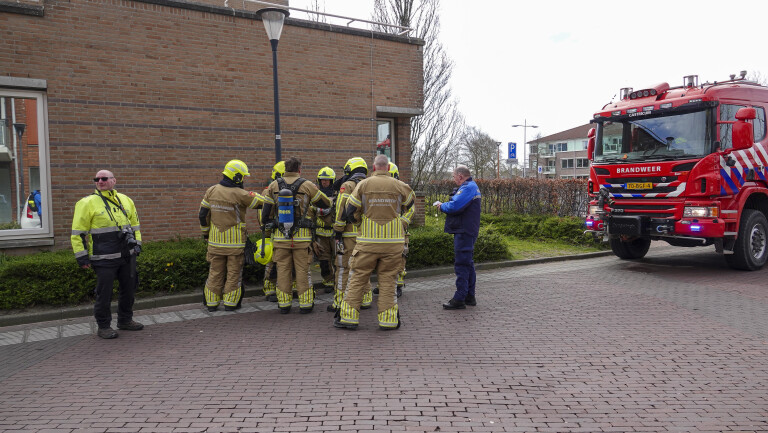 Brandweermensen staan buiten bij een bakstenen gebouw naast een geparkeerde brandweerwagen met "BRANDWEER" op de voorkant.