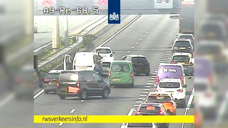 Een file op de snelweg A9 met meerdere auto's, waaronder enkele bestelwagens, waarbij een man zichtbaar uit een witte bestelwagen is gestapt.