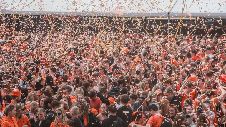 Een grote menigte gekleed in oranje viert feest met confetti en slingers in de lucht.