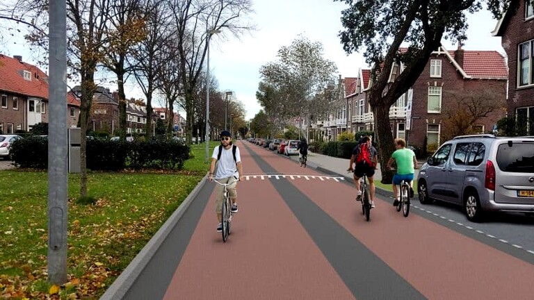Een rustige straat in een woonwijk met een fietser op een fiets aan de linkerkant en twee fietsers aan de rechterkant. Beide kanten van de straat zijn omgeven door bomen en bakstenen huizen met rode daken. Auto's staan geparkeerd langs de weg.