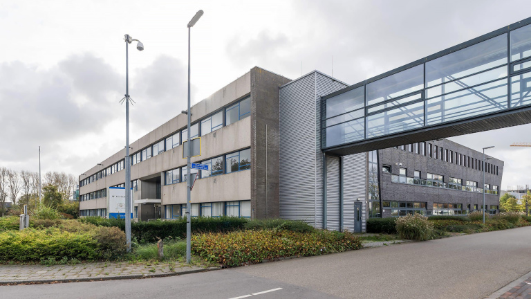 Kantoor- of bedrijfsgebouwen met een glazen loopbrug tussen beide gebouwen, gelegen aan een rustige weg met groenvoorzieningen.