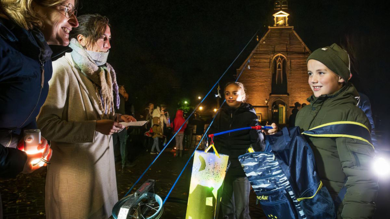 Kinderen en volwassenen dragen lampionnen tijdens een evenement in de avond bij een verlichte kerk.