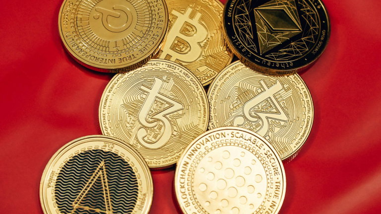 Een stapel gouden munten met logo's van verschillende cryptocurrency's zoals Bitcoin, Ethereum, en Tezos op een rode achtergrond.