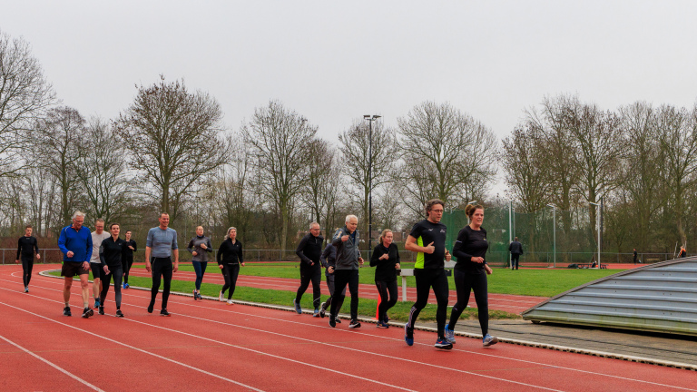 Een groep mensen loopt en jogt op een atletiekbaan omgeven door kale bomen.