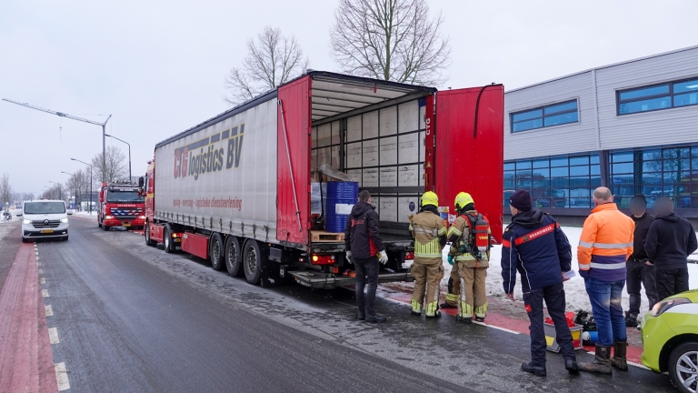Brandweerlieden en andere personen staan bij een geopende vrachtwagen op een besneeuwde weg, naast een bedrijfspand.