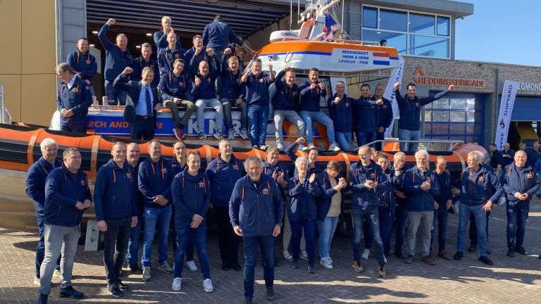 Groep mensen poseert voor een reddingsboot bij de KNRM-reddingsbrigade.