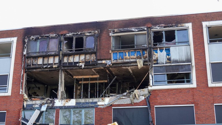 Bovenverdieping van een appartementsgebouw met ernstige brandschade; kapotte ramen, zwartgeblakerde muren en instortende constructies zijn zichtbaar.