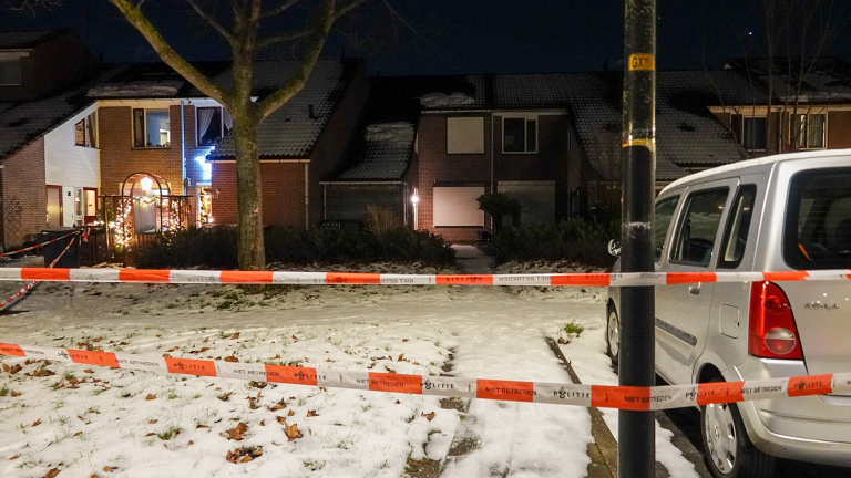 Huis met kerstverlichting is afgezet met politielint, omgeven door sneeuwbedekte grond en een geparkeerde auto.