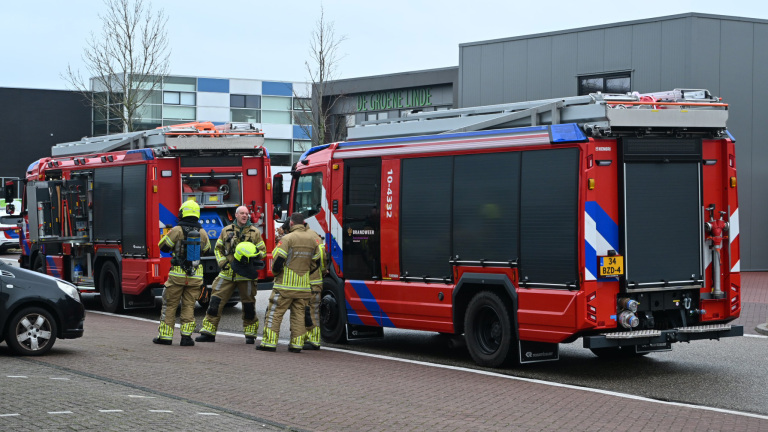Brandweerlieden naast twee geparkeerde Nederlandse brandweerwagens in een stedelijke omgeving.