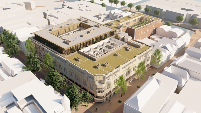 Luchtfoto van een gebouw met een groene daktuin, omgeven door bomen en straten, met de naam "Vroom & Dreesmann" op de gevel.