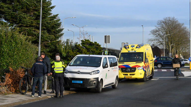 Twee politieagenten praten met mannen naast een bestelwagen en een ambulance, terwijl een fietser langsrijdt.