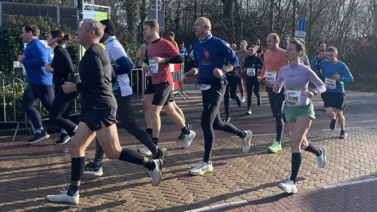 Hardlopers in sportkleding rennen op een straat omringd door toeschouwers en verkeersborden.