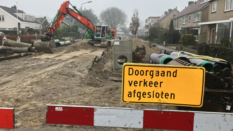 Een straat met wegwerkzaamheden, grote buizen en graafmachines, met een bord "Doorgaand verkeer afgesloten".