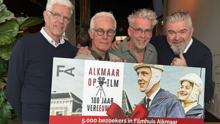 Vier mannen poseren met een poster van "Alkmaar op Film" voor 5.000 bezoekers in het Filmhuis Alkmaar.