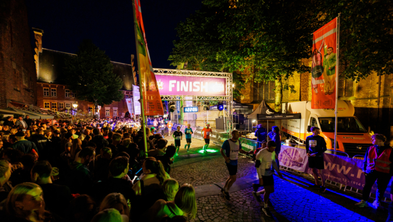 Hardlopers halen de finish bij een nachtelijke run met veel toeschouwers en kleurrijke verlichting in de straten.
