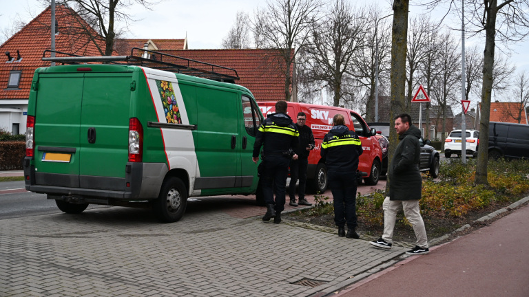 Politieagenten staan bij een groene en een rode bestelwagen naast een trottoir, terwijl een man toekijkt.