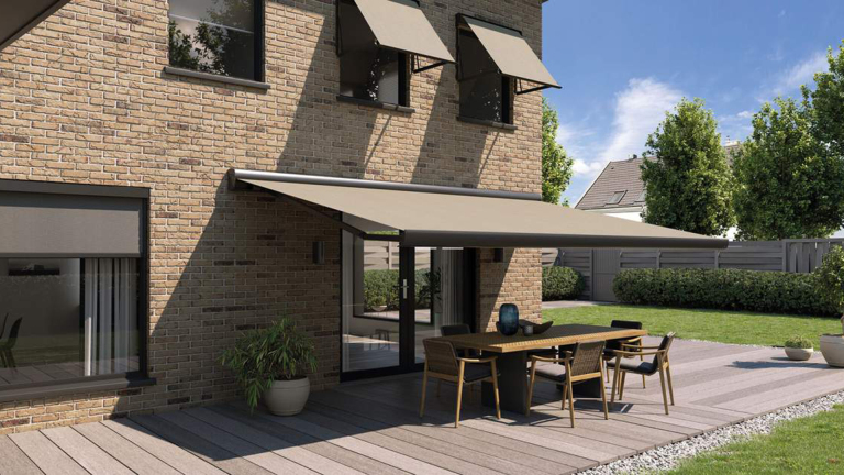 Terrastafel met zes stoelen onder een beige zonnescherm tegen een bakstenen huis, met tuin op de achtergrond.