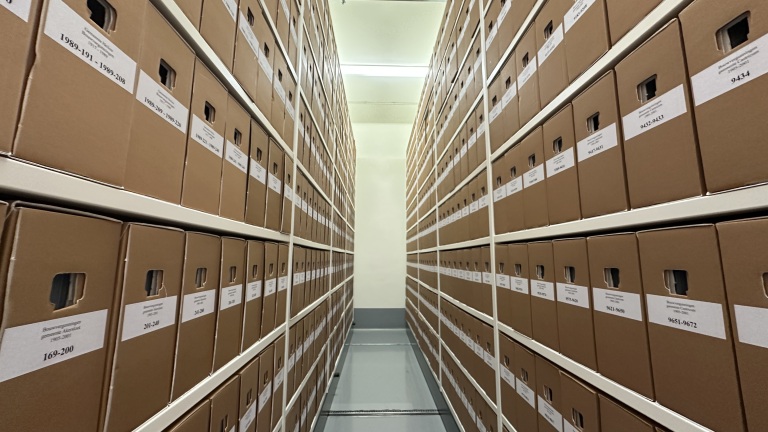 Gang met archiefdozen netjes gestapeld in hoge rekken aan beide kanten.