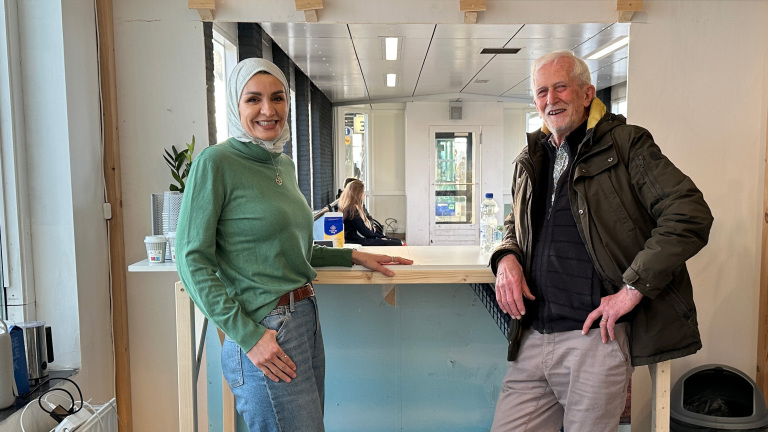 Een vrouw en een man glimlachen en leunen ontspannen tegen een toonbank in een moderne ruimte.