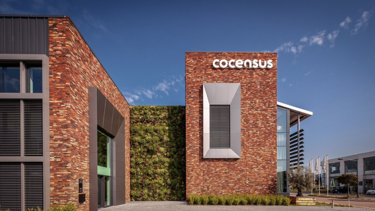 Bakstenen gebouw met "Cocensus" op de gevel, een groene geveltuin en moderne architectuur onder een blauwe hemel.