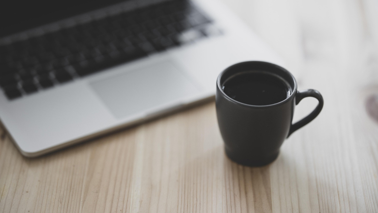 Zwarte koffiekop naast een laptop op een houten tafel.