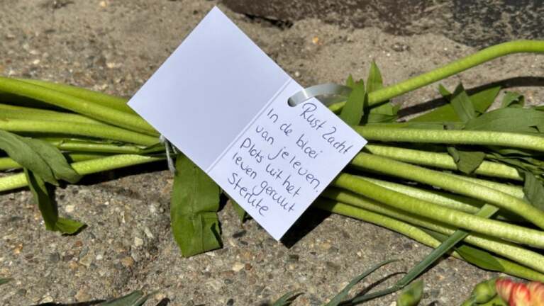 Bloemen met een kaartje waarop staat: "Rust zacht. In de bloei van je leven plots uit het leven gerukt. Sterkte."