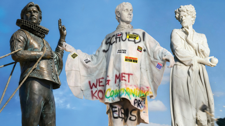 Drie standbeelden, waarvan één met graffiti en stickers met teksten als "Decolonize Now" en "Justice For All" erop.