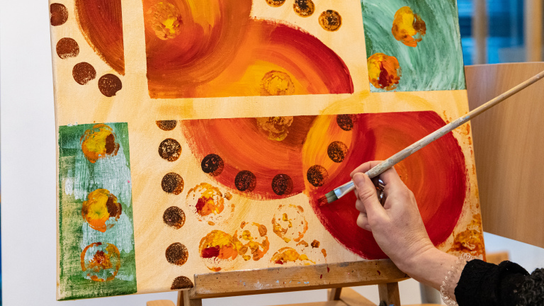 Een hand schildert een abstract schilderij met cirkelvormige patronen in rood, geel en groen.