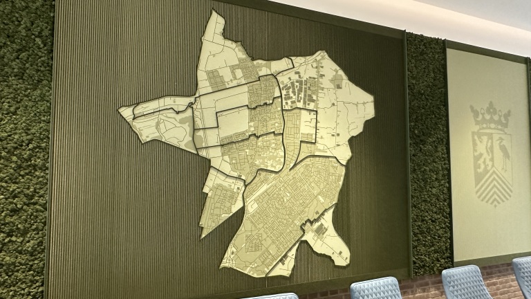 Wanddecoratie met een reliëfkaart van een stadsplattegrond, omgeven door groene texturen, en naast een wapenschild.