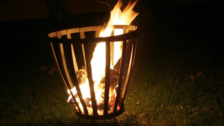 Een fakkelkorf buiten gevuld met brandend hout op een grasveld in de nacht.