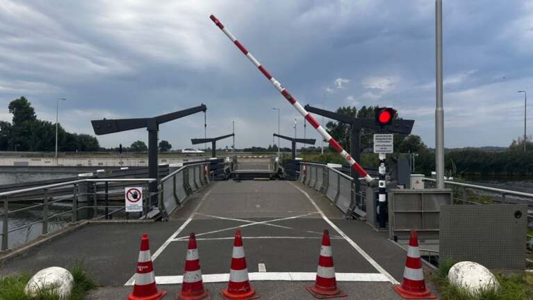Wegversperring bij een open brug met slagbomen omhoog, verkeerslichten op rood en vier verkeerskegels op de voorgrond.