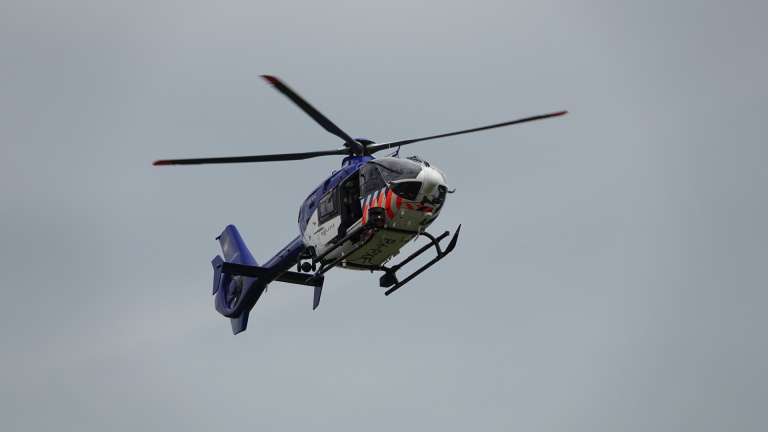 Een politiehelikopter in de lucht met draaiende rotorbladen tegen een grijze hemel.