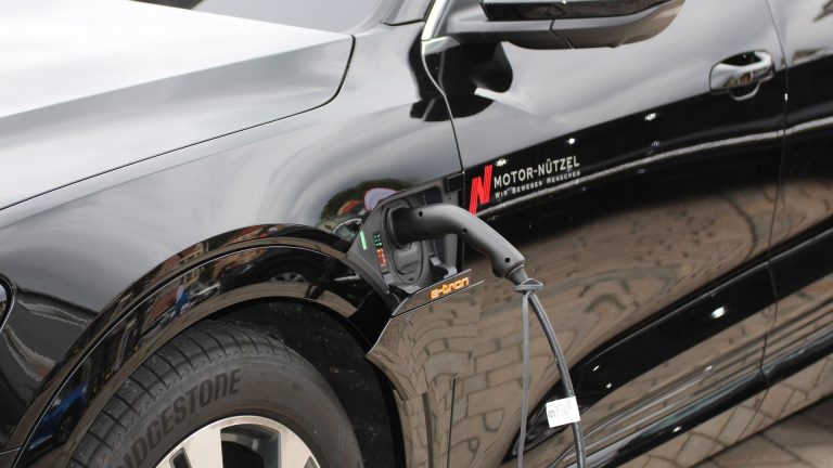 Close-up van een zwarte elektrische auto die wordt opgeladen via een laadkabel aan de zijkant.