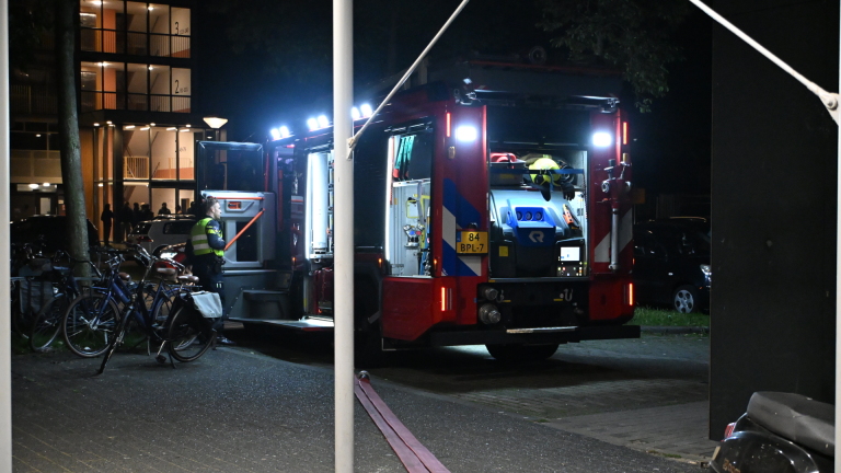 Brandweerwagen bij nacht voor een gebouw, naast geparkeerde fietsen, met een medewerker in uniform ernaast.