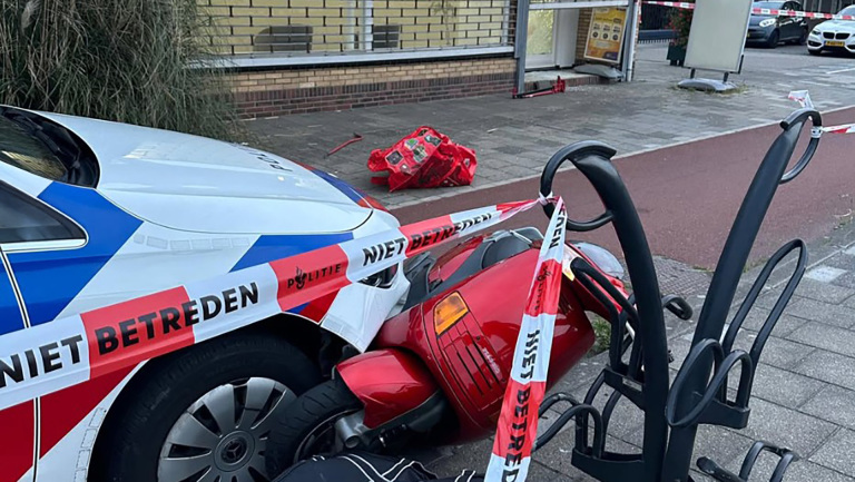 Een politieauto heeft een rode scooter aangereden, omgeven door afzetlint met "NIET BETREDEN".