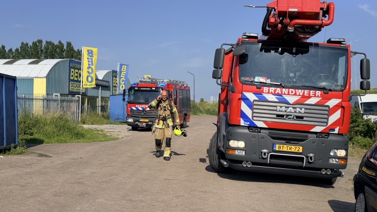 Brandweerwagen en brandweerman naast een garage met BECO-borden, onder een heldere blauwe lucht.
