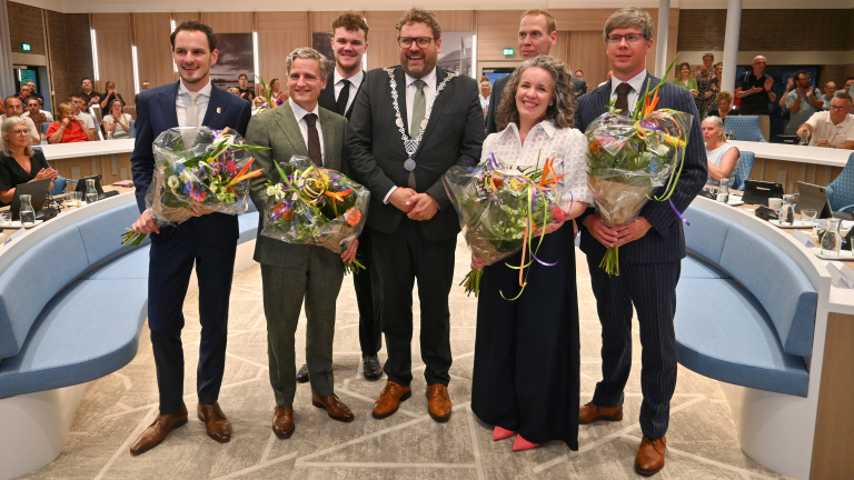 Groep mensen in een ceremoniezaal, sommigen met bloemen in de hand, een man draagt een ambtsketen.