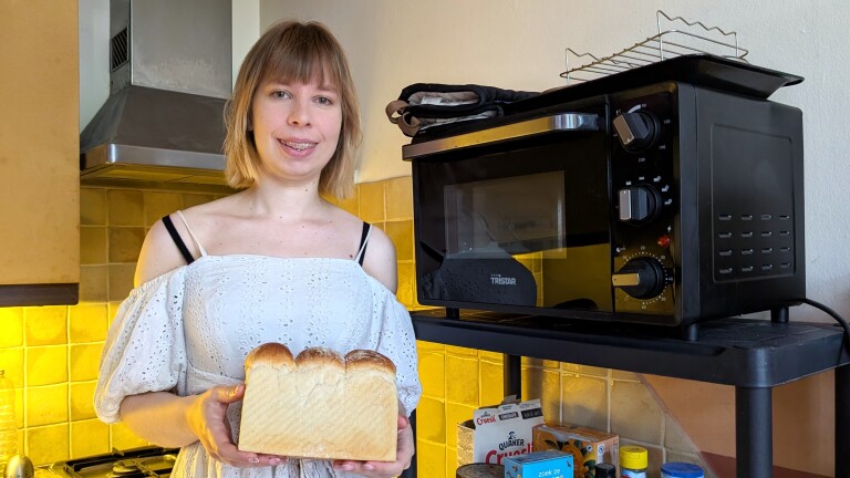 Vrouw in de keuken houdt zelfgebakken brood vast naast een zwarte oven.