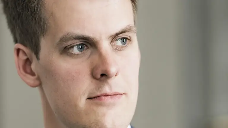 Een man kijkt uit het raam, wat een lichte, neutrale achtergrond.