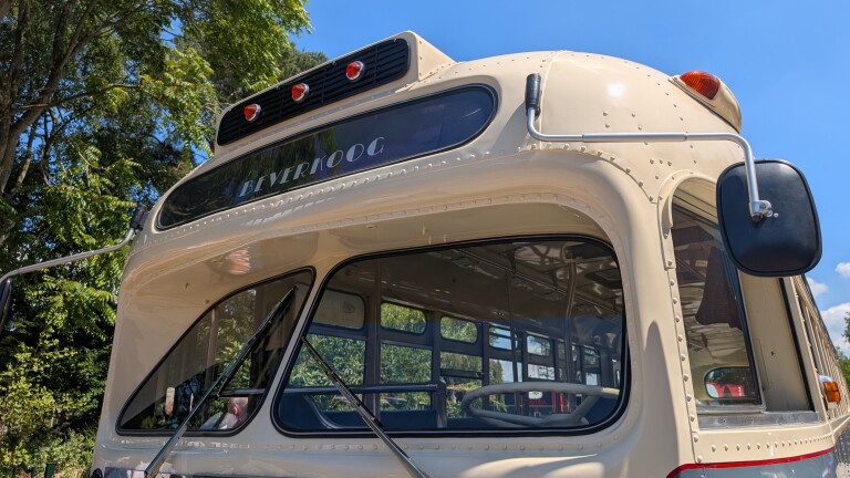Voorkant van een vintage bus met de tekst "BEVERKOOG" op de bestemming, omringd door groene bomen en een blauwe hemel.