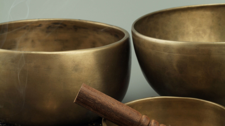Twee bronzen klankschalen met een houten klopper op de voorgrond.