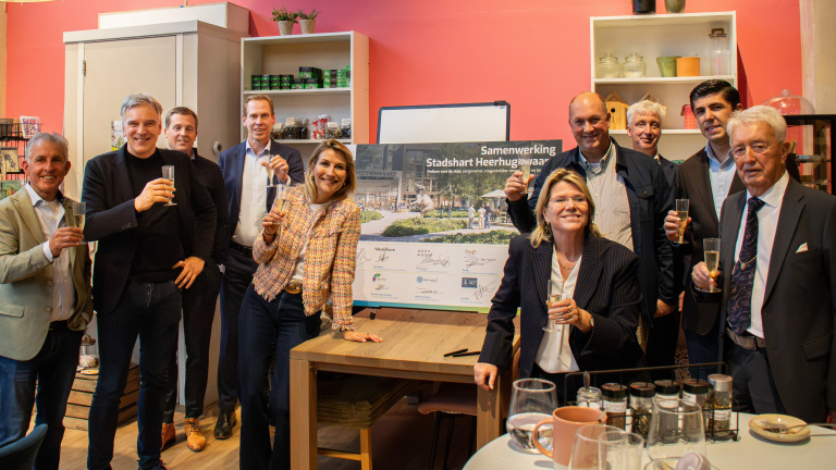 Groep mensen proost met champagneglazen bij bord met tekst Samenwerking Stadshart Heerhugowaard