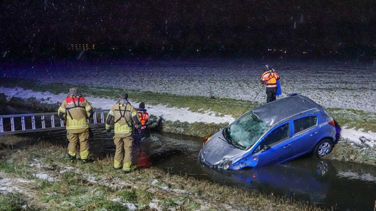 Brandweerlieden redden mensen uit een auto die scheef in een besneeuwde sloot ligt.