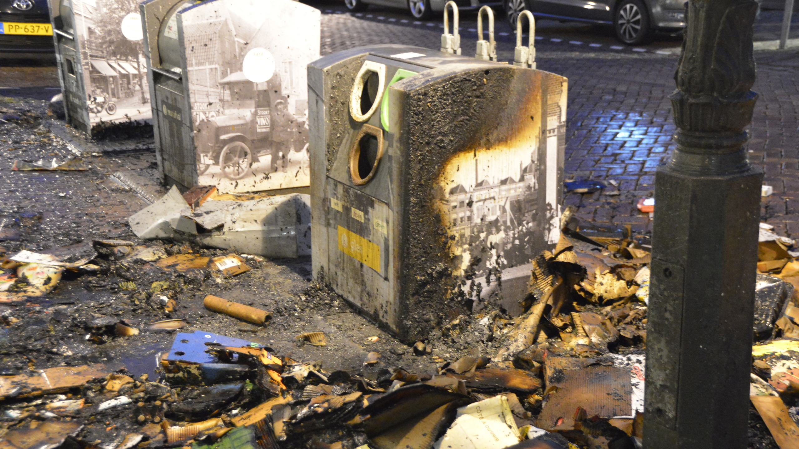 Afvalhopen van kartonnen dozen en puin op een natte straat naast een brandweerwagen en dicht bij een winkel.